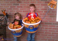 two children dressed in costumes standing next to each other holding buckets of hot dogs