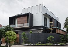 a modern house with trees and shrubs in front of it on a cloudy day,