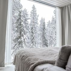 a bed sitting in front of a window covered in snow next to a forest filled with trees