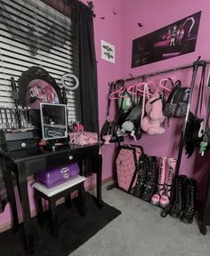 a room with pink walls, black furniture and lots of clothes hanging on the rack