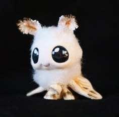 a white stuffed animal with black eyes sitting on top of a black cloth covered surface