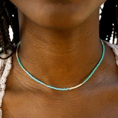 a woman wearing a blue and white beaded necklace on her neck with braids