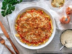 a white bowl filled with pasta and sauce on top of a table next to utensils