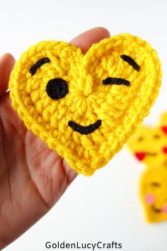 a crocheted smiley face is held up in front of two small yellow hearts