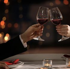 two people toasting with red wine in front of candles on a dining room table