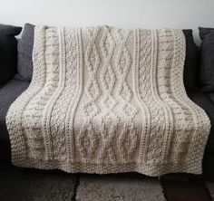 a white knitted blanket sitting on top of a black couch next to a wall