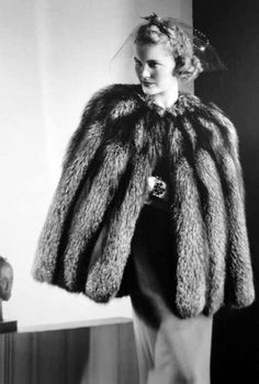 a woman in a fur coat standing next to a table