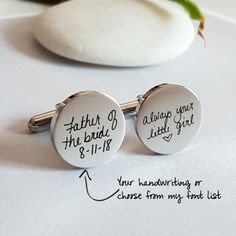 two cufflinks with handwriting on them sitting next to a white piece of paper