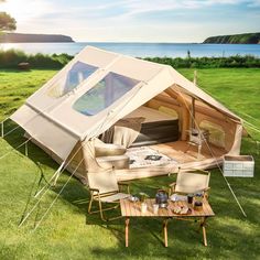 a tent set up on the grass with chairs and tables in front of it next to water