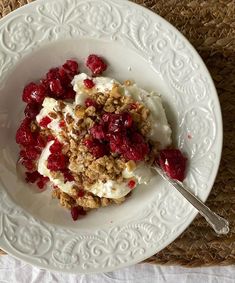 a white plate topped with granola and fruit next to a spoon on a table