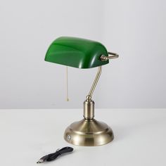 a green desk lamp sitting on top of a white table next to a charger