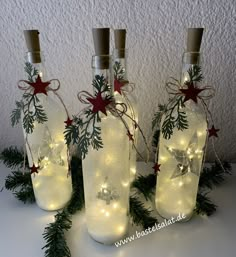 three glass bottles with lights in them are sitting on a table next to evergreen branches