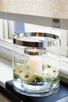 a candle and flowers in a glass container on a window sill