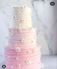 a three tiered cake with white flowers on the top and pink frosting in the middle