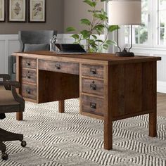 a wooden desk sitting on top of a rug next to a chair and table with a lamp