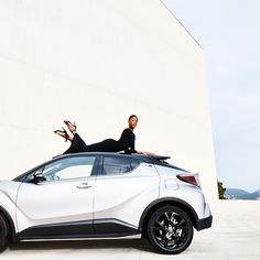 two people sitting on the roof of a white car with black rims and wheels