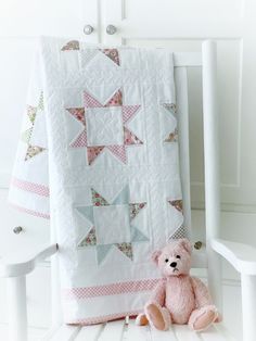 a pink teddy bear sitting in front of a quilt on a white chair next to it