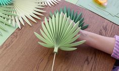 a person holding a green paper fan on top of a wooden table next to other items