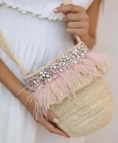 a woman is holding a purse with pink feathers and beads on the handle, while wearing a white dress