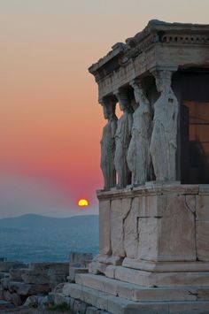 the sun is setting behind some statues on top of a hill with mountains in the background