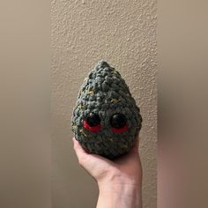 a hand holding a crocheted rock with red eyes