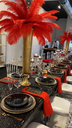 a table set up with black and gold place settings, red feather centerpieces