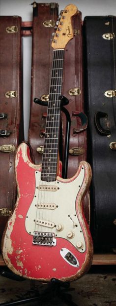 an old red guitar sitting on top of a wooden shelf next to other suitcases