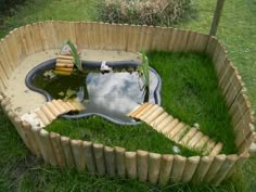 a pond made out of bamboo sticks in the middle of a yard with grass around it