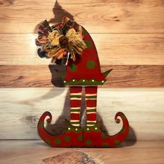 a red and green christmas decoration sitting on top of a wooden floor next to a wall