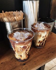 two glasses filled with ice cream sitting on top of a wooden table next to drinks