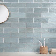 a mirror and toothbrush holder in front of a blue brick wall with a round mirror above it