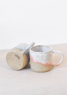 two mugs sitting on top of a wooden table next to each other, one with a straw lid