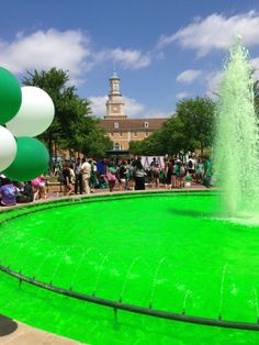 a large green fountain surrounded by balloons in front of a building with a clock tower