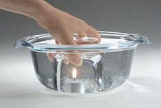 a hand reaching into a glass bowl with water on the bottom and light in it