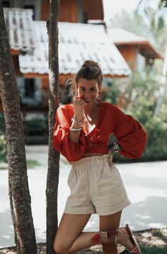 a woman standing next to a tree talking on a cell phone while wearing high heels