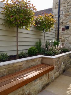 a wooden bench sitting next to a stone wall and planter filled with flowers on the side of a building