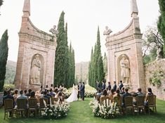 a wedding ceremony in front of an old stone building with statues and flowers on the lawn