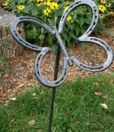 a metal butterfly sculpture sitting on top of a green grass covered field next to yellow flowers