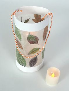 a candle is sitting next to a cup with leaves on it and a string around it