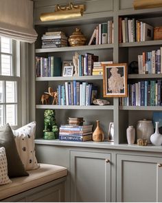 a bookshelf filled with lots of books next to a window covered in pillows