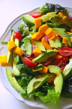 a salad with avocado, tomatoes and lettuce on a white plate