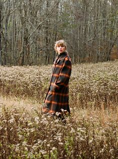 a woman standing in the middle of a field wearing a plaid coat and black boots