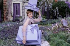 a woman is holding two boxes on her head in the middle of a garden with purple flowers