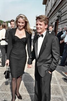 a man and woman dressed in formal wear walking down the street holding hands with each other