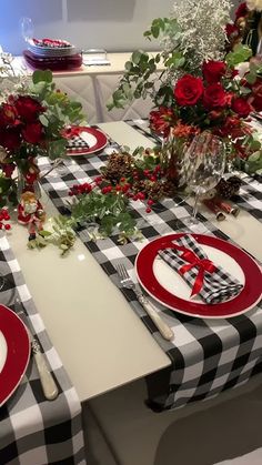 the table is set for christmas dinner with red and black plates, napkins and flowers