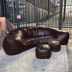 a brown leather couch sitting on top of a white rug next to a metal fence