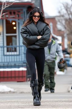 a woman in black leggings and boots is walking down the street with her arms crossed