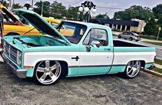 a turquoise and white truck parked in a parking lot next to other cars on the street