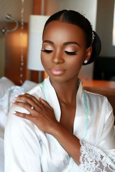 a woman in a white robe with her hands on her chest, wearing a tiara