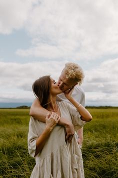 a man and woman are kissing in the middle of an open field with tall grass